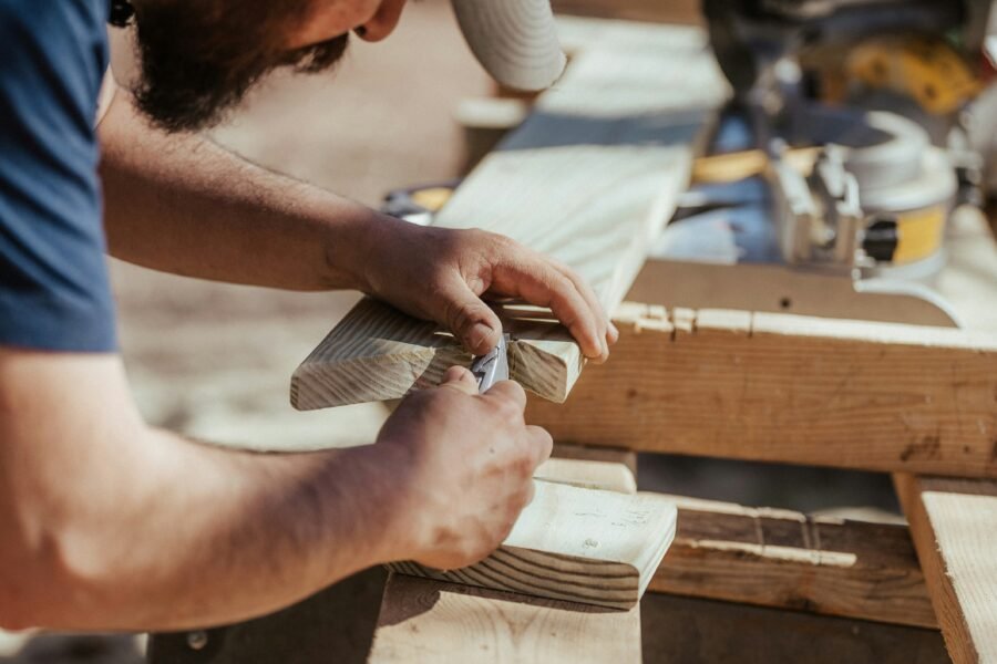 Close-up of hands measuring and marking a wood plank with a tool