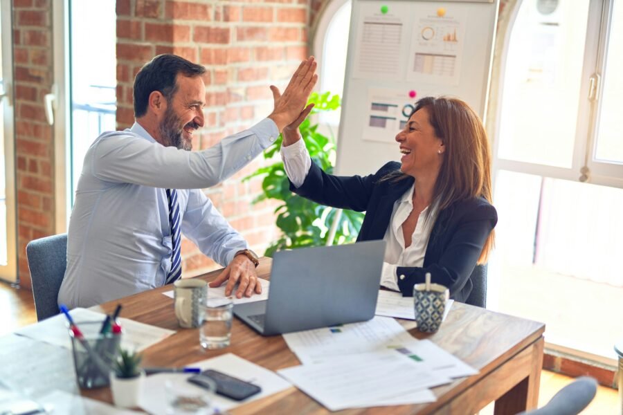 Two business professionals high-fiving over a desk with a laptop